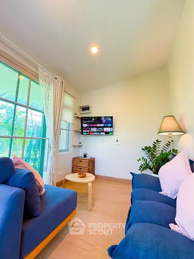 Cozy living room with blue sofas, wall-mounted TV, and large window with garden view.