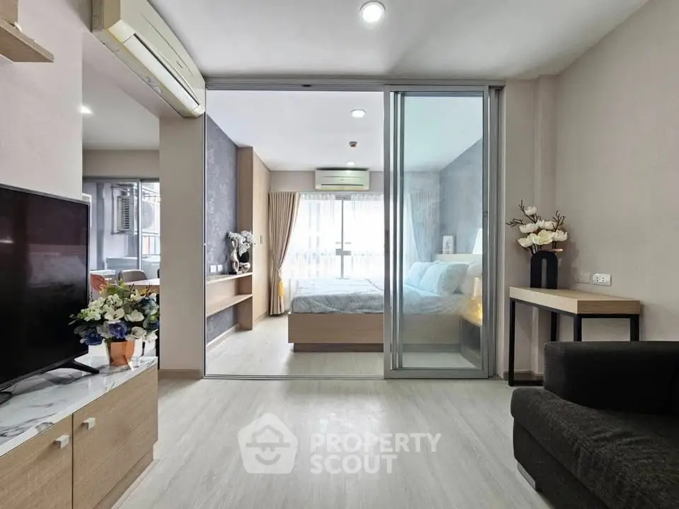 Modern living room with sliding glass doors leading to a cozy bedroom, featuring stylish decor and ample natural light.