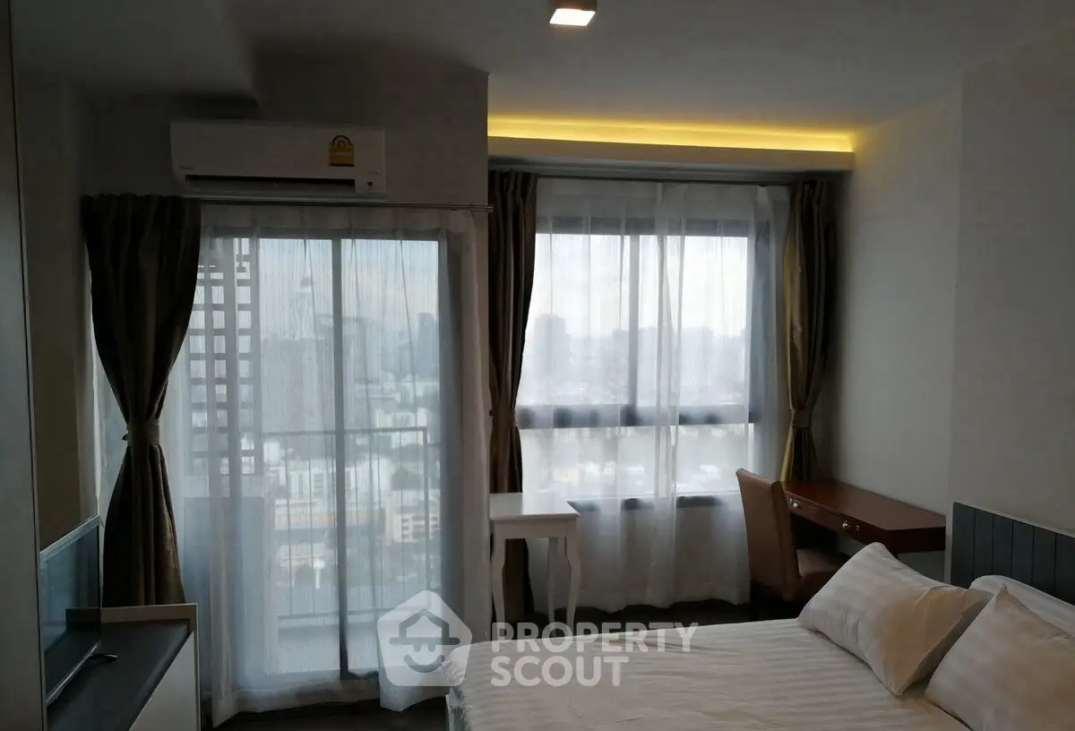 Modern bedroom with city view, featuring large windows and elegant furnishings.