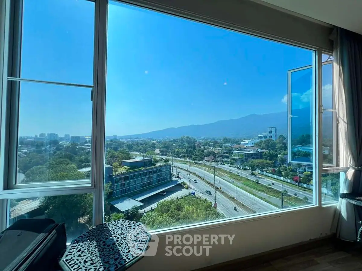 Stunning panoramic view from high-rise apartment window overlooking cityscape and mountains.