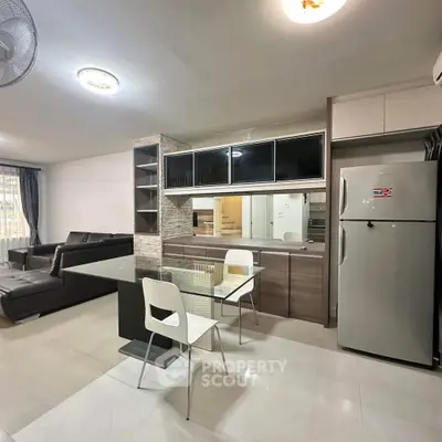 Modern open-plan living room with sleek kitchen and dining area, featuring contemporary furniture and appliances.