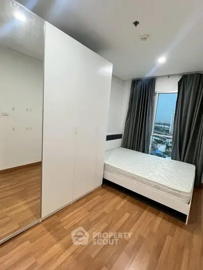 Modern bedroom with wooden flooring and city view, featuring a sleek wardrobe and comfortable bed.