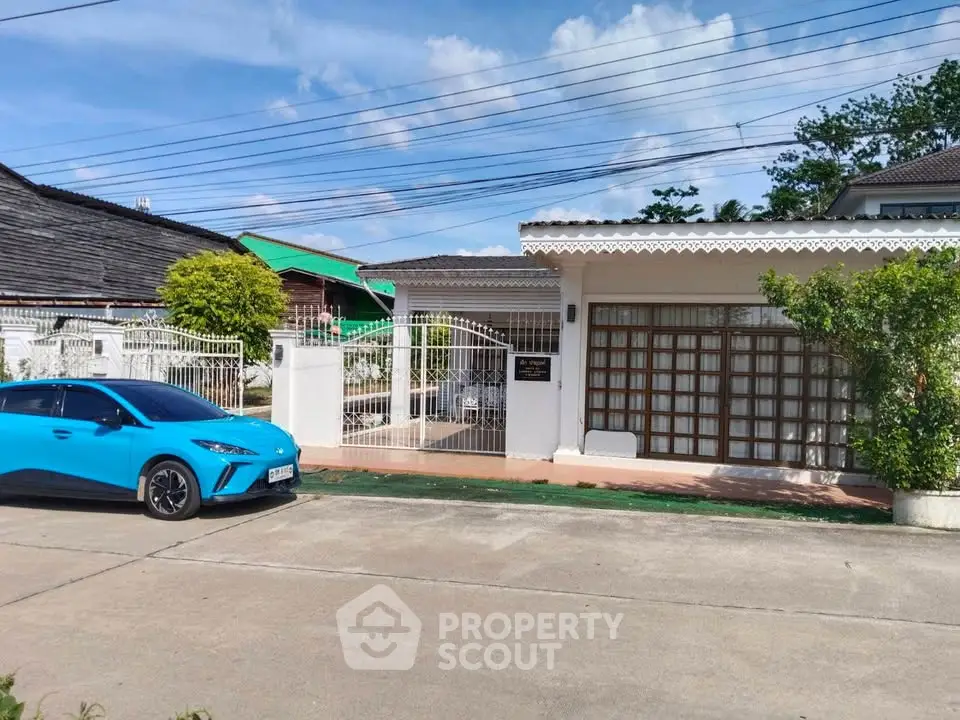 Charming suburban home with gated entrance and driveway, featuring a vibrant blue car parked outside.