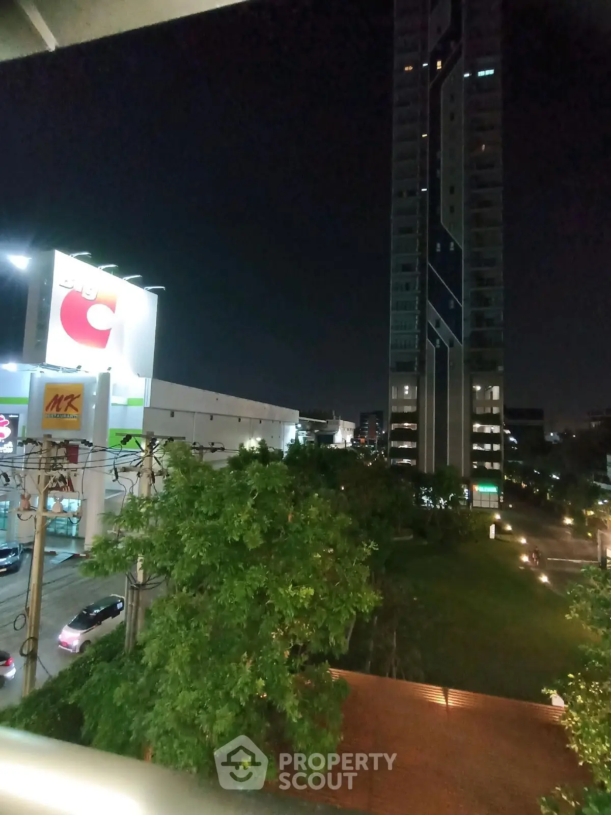 Night view of modern high-rise building with lush greenery and illuminated surroundings.