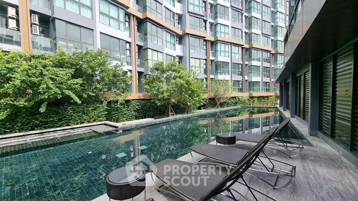 Luxurious modern apartment complex with serene poolside view and lush greenery.