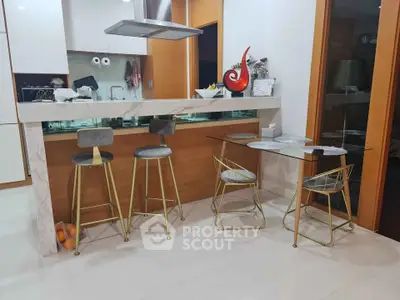 Modern kitchen with sleek bar stools and glass dining table, featuring a stylish open layout and contemporary design.