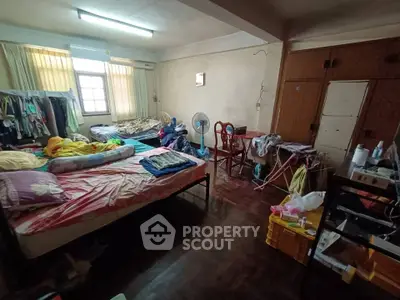 Spacious bedroom with wooden flooring and ample natural light, featuring a cozy setup with multiple beds and storage.