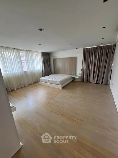 Spacious bedroom with large windows and wooden flooring, featuring a minimalist design and ample natural light.