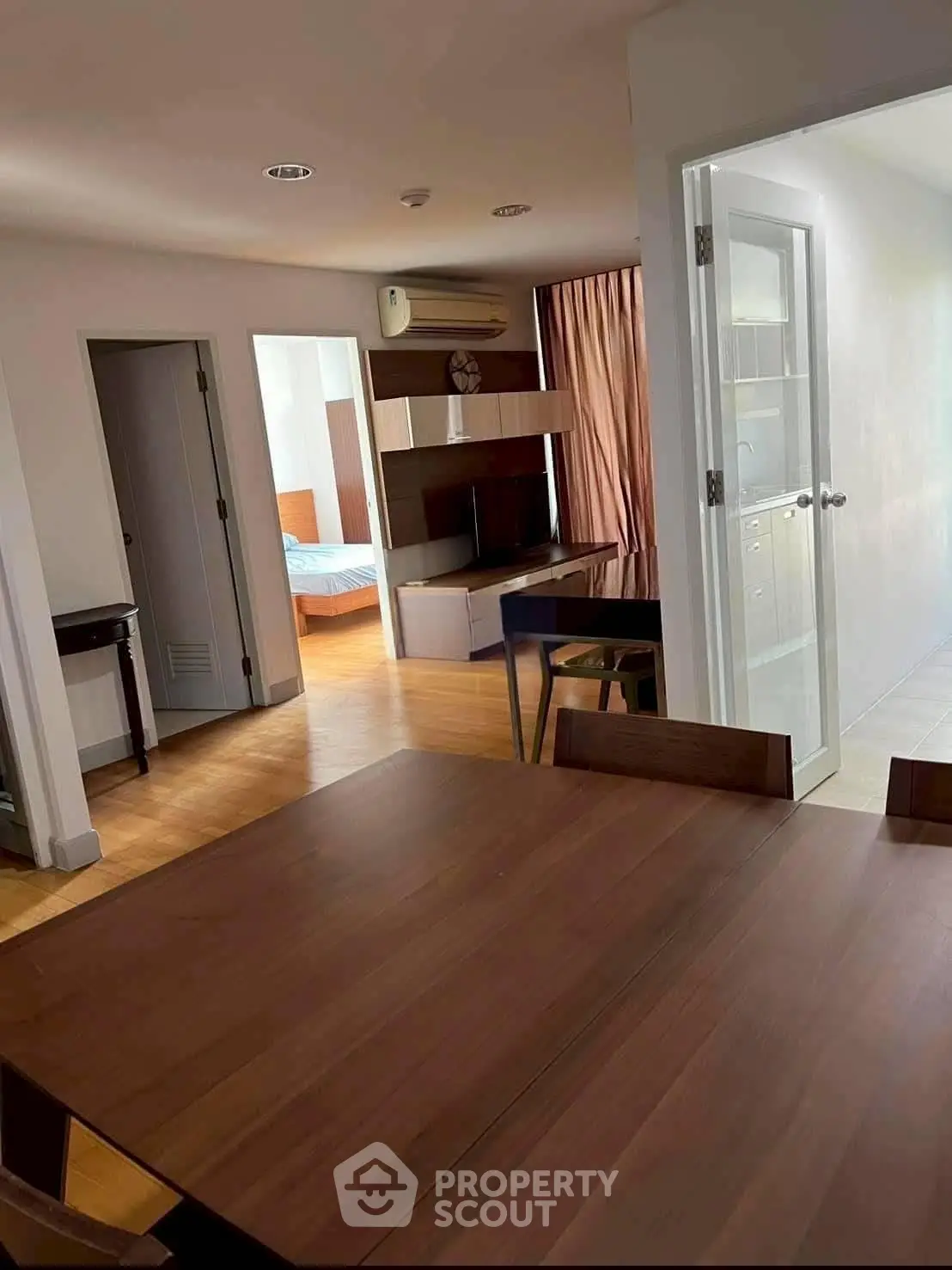 Spacious open-plan living area with wooden dining table and modern decor, leading to a cozy bedroom.