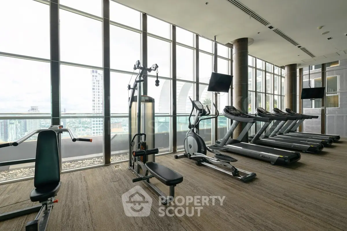 Spacious modern gym with city view, featuring state-of-the-art exercise equipment and floor-to-ceiling windows.