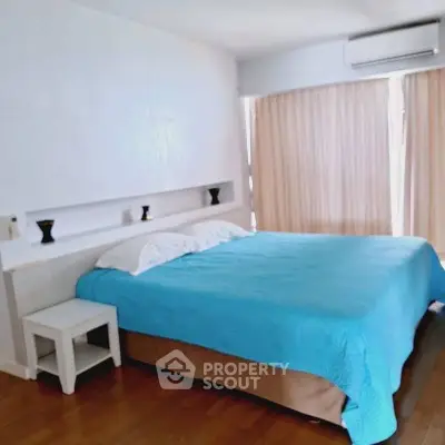 Spacious bedroom with blue bedding and natural light, featuring modern decor and air conditioning.