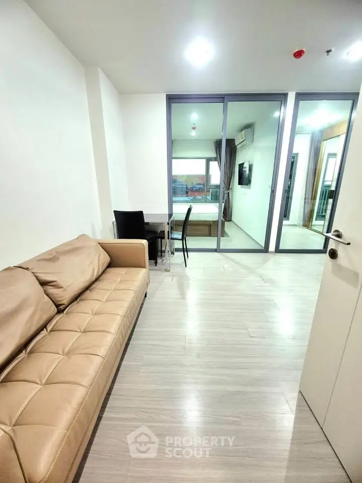 Modern living room with beige sofa and glass partition leading to a balcony with city view.