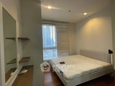 Spacious bedroom with large window and modern furnishings in a high-rise apartment.