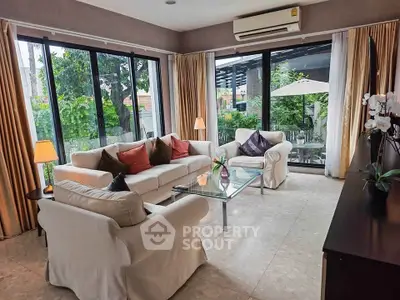 Spacious living room with large windows and garden view, featuring elegant sofas and modern decor.