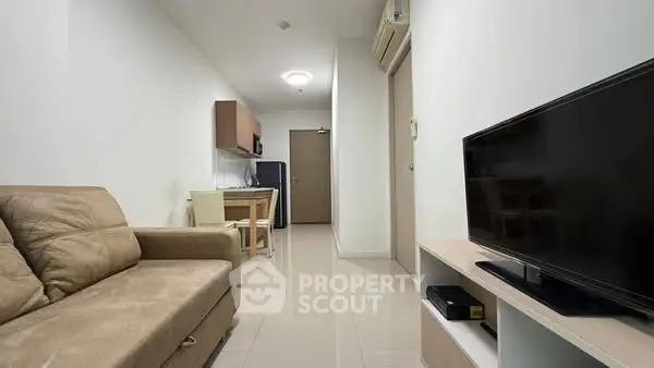 Modern living room with beige sofa and flat-screen TV, open to compact kitchen area.