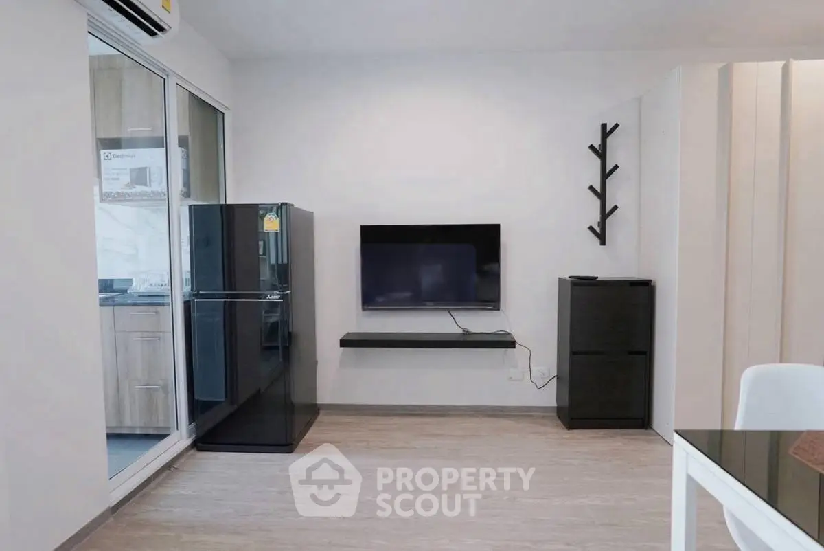 Modern living room with sleek black furniture and wall-mounted TV, adjacent to a stylish kitchen.