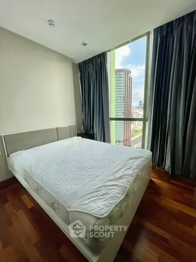 Spacious bedroom with large window offering stunning city views, featuring elegant wooden flooring.