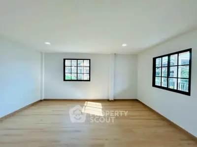 Spacious empty room with wooden flooring and large windows for natural light.