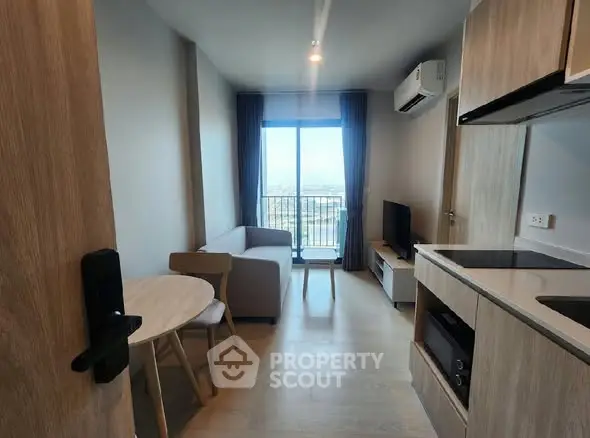 Modern living room with balcony view, compact kitchen, and cozy seating area.