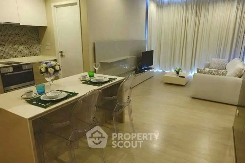 Modern open-plan living room with kitchen, featuring sleek decor and natural light.