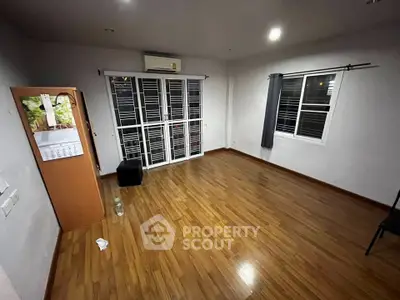 Spacious empty room with wooden flooring and large windows, perfect for customization.