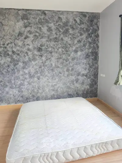 Minimalist bedroom with textured gray wall and mattress on wooden floor