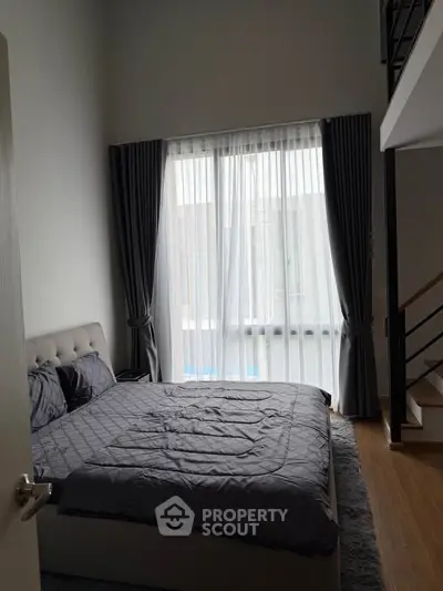 Spacious bedroom with high ceiling and modern decor, featuring a large window with elegant curtains.