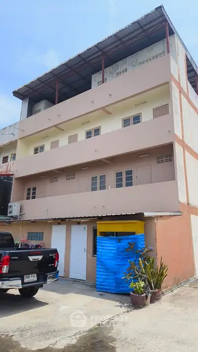 Three-story building with parking space and plants, ideal for commercial or residential use.