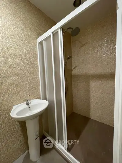Modern bathroom with sleek shower enclosure and pedestal sink, featuring neutral tile design.