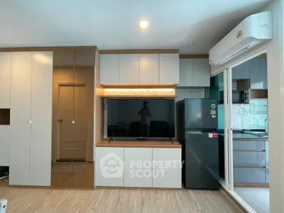 Modern living room with sleek cabinetry, flat-screen TV, and stainless steel fridge in a stylish apartment.