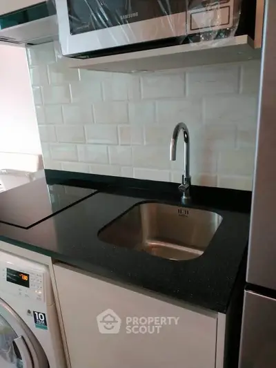 Modern kitchen with sleek black countertop, built-in microwave, and washing machine for efficient living.