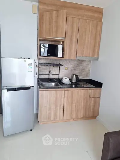 Modern compact kitchen with wooden cabinets and stainless steel appliances in a cozy apartment.