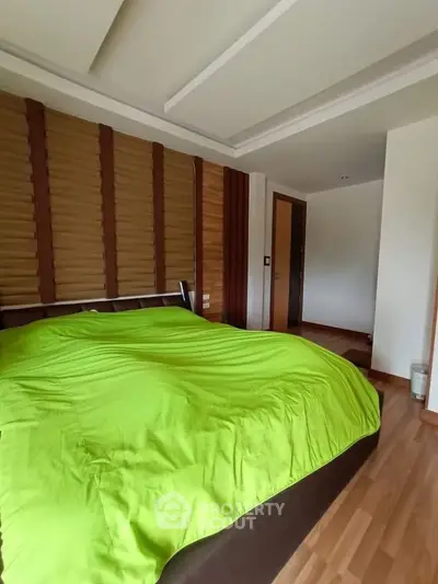 Spacious bedroom with modern design and vibrant green bedding, featuring wooden flooring and stylish wall accents.