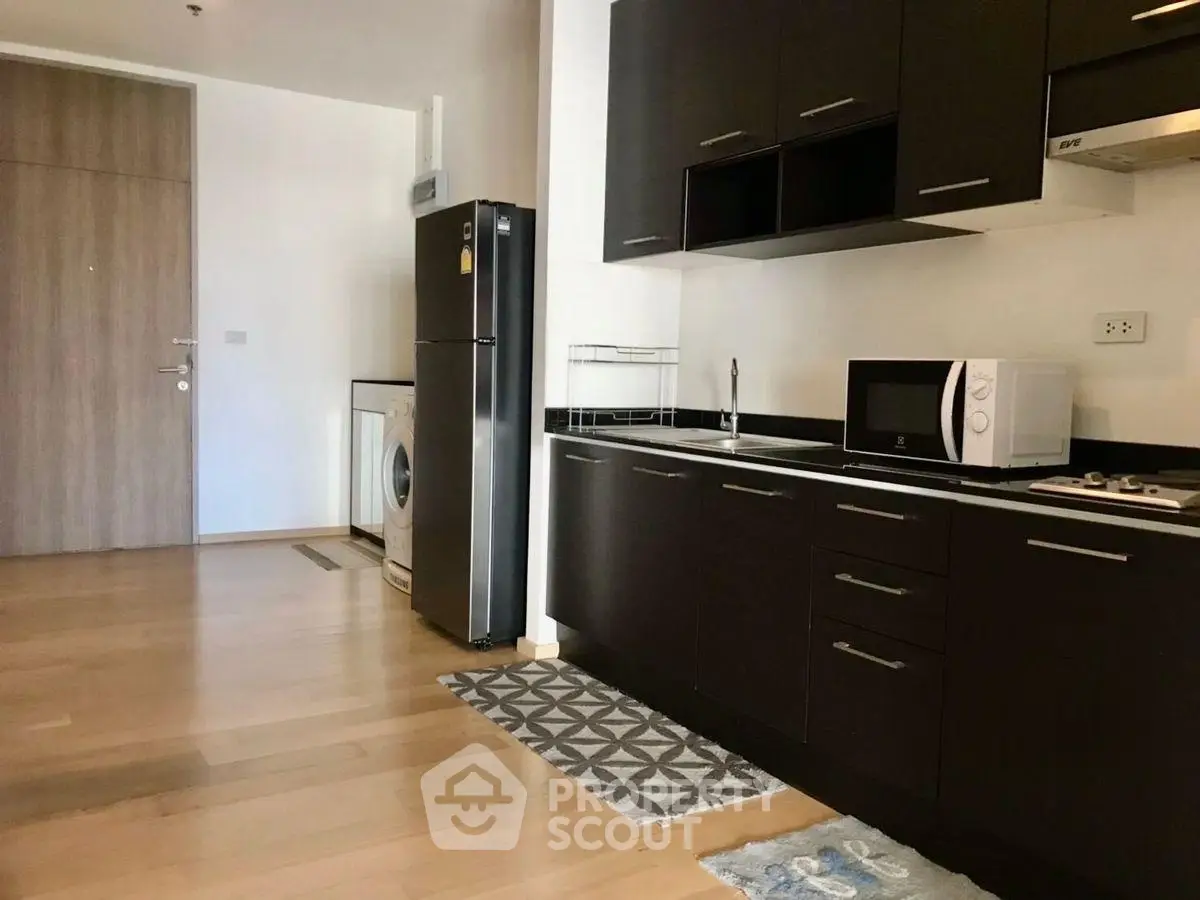 Modern kitchen with dark cabinets, fridge, and washing machine in open layout apartment.