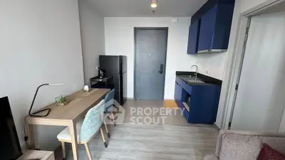 Modern apartment interior with sleek kitchen and dining area, featuring stylish blue cabinetry and contemporary furniture.