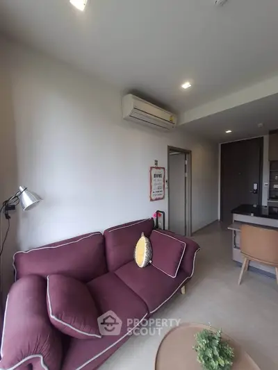 Modern living room with stylish maroon sofa and open kitchen layout in a cozy apartment.