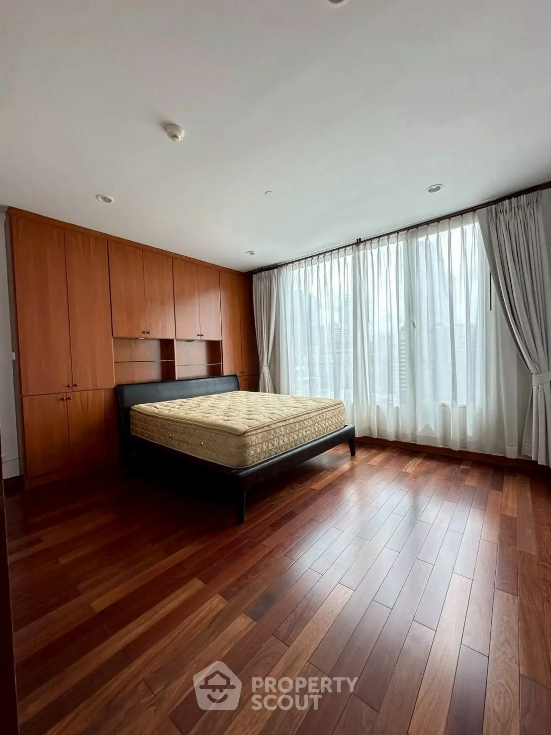 Spacious bedroom with wooden flooring and large windows for natural light.