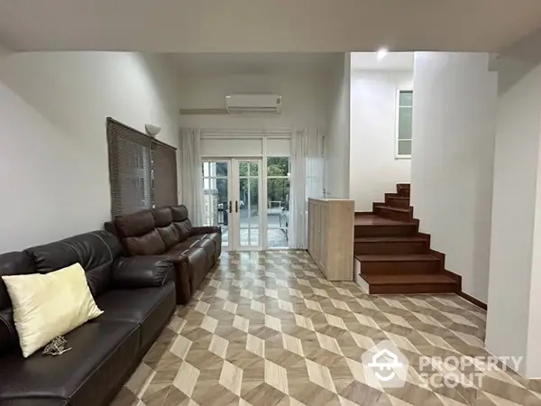 Spacious living room with elegant tiled flooring, comfortable leather sofa, and direct access to a bright staircase leading to upper levels.