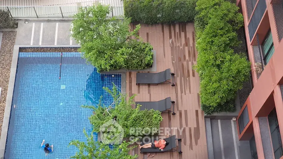 Stunning aerial view of modern apartment pool area with lush greenery and sun loungers.