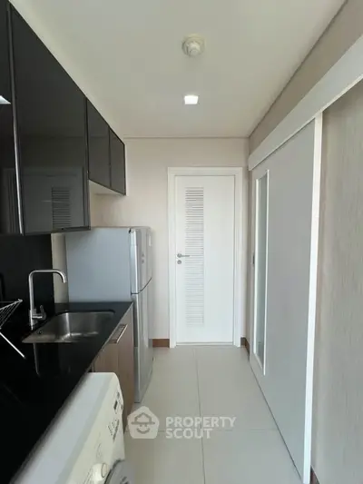 Modern kitchen with sleek black cabinets, stainless steel fridge, and washing machine in a compact layout.