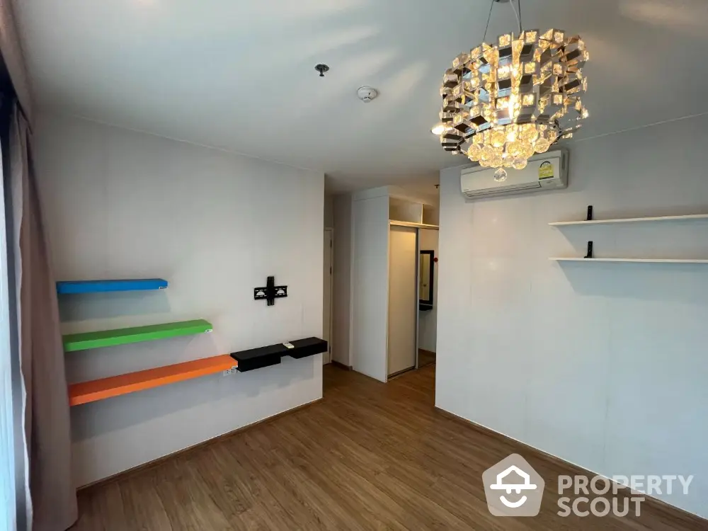 Modern minimalist living room with vibrant floating shelves and an elegant chandelier, featuring sleek wooden flooring and ample natural light.