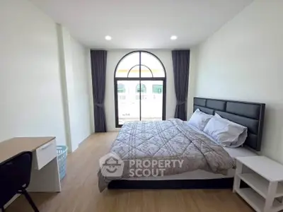 Spacious bedroom with large window and modern furnishings in a bright apartment.