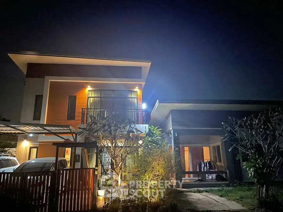 Modern two-story house with illuminated exterior and lush garden at night.