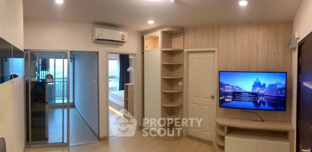 Modern living room with built-in shelves and wall-mounted TV, leading to a balcony with city view.