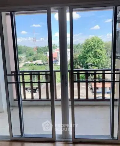 Spacious balcony with sliding glass doors offering a scenic view of lush greenery and clear skies.