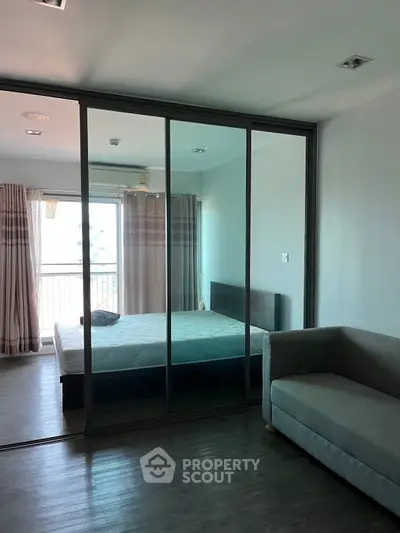 Modern bedroom with glass partition and cozy sofa, featuring natural light and stylish decor.
