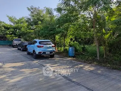 Spacious parking area surrounded by lush greenery and parked cars.