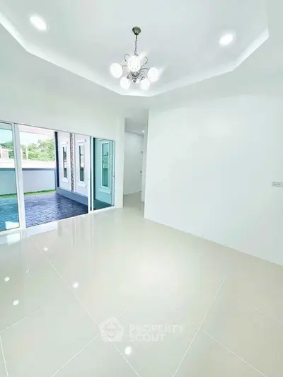 Spacious modern living room with elegant chandelier and large windows opening to a patio.