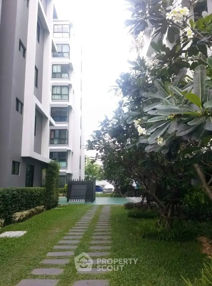 Modern apartment building with lush garden pathway and vibrant greenery.