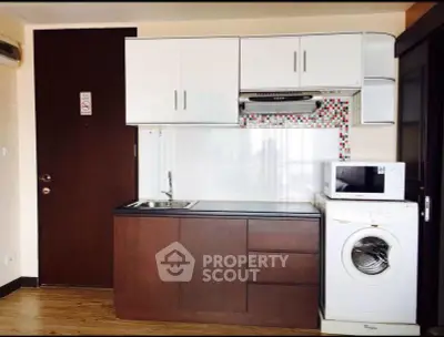 Compact kitchen with modern appliances including washing machine and microwave, featuring sleek cabinetry.